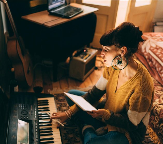 Girl with brown hair and fringe playing keyboard in bedroom