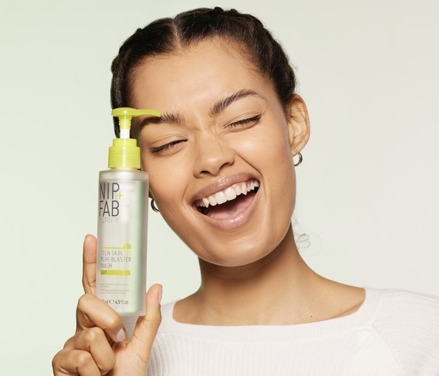 A mixed race girl in a white top smiling open mouthed with her head at an angle.  Holding a bottle