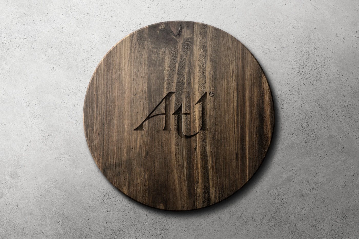 At1 logo etched in to a dark wooden disc aganst a concrete background