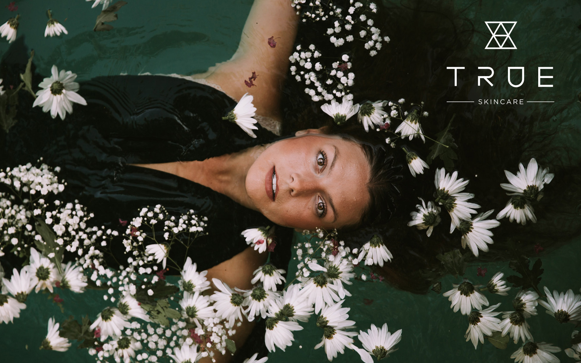 Woman laying in water surrounded by flowers