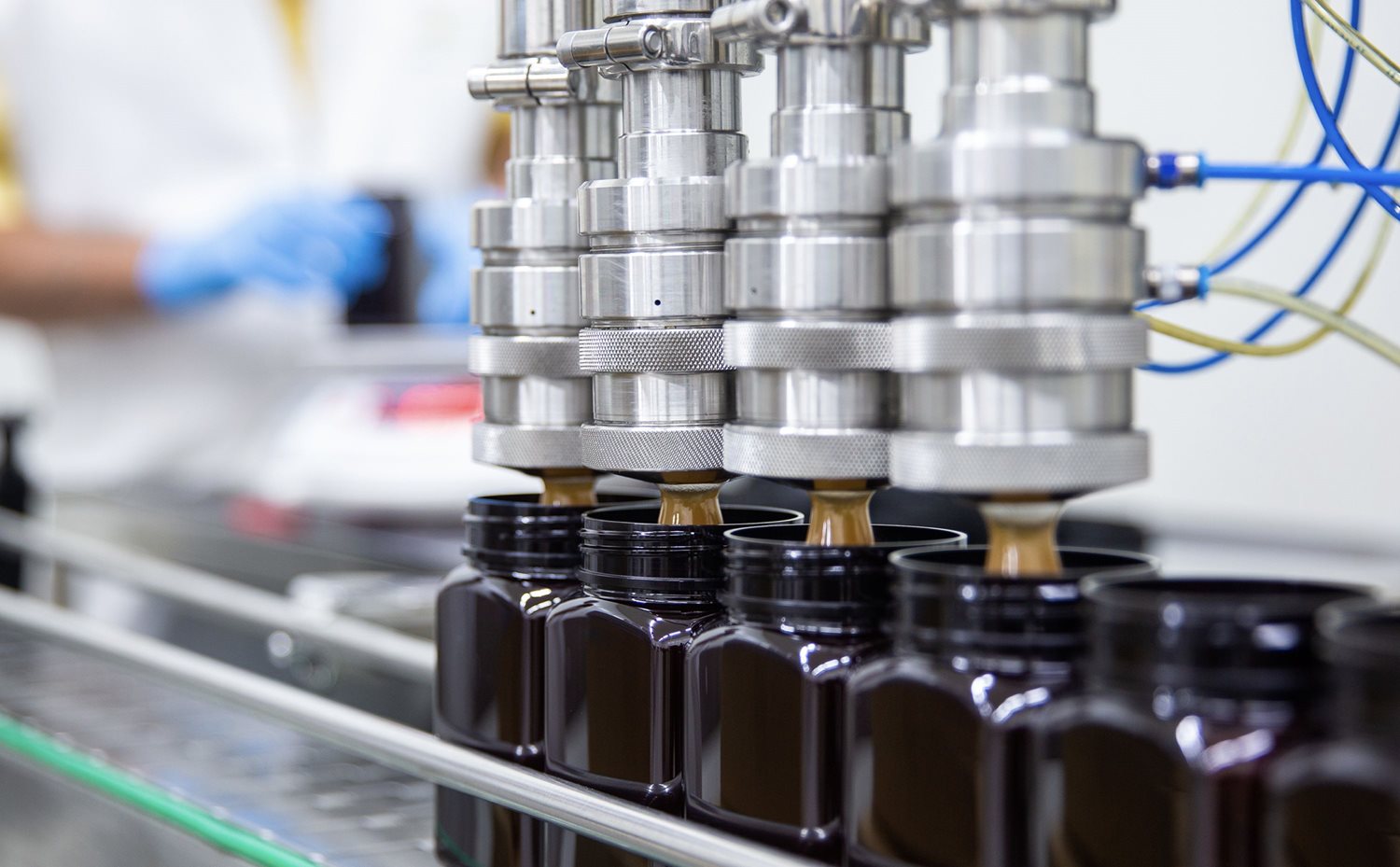 A close up shot of some equipment. A row of four chrome cylinders with nozzles.  They are depositing honey in to jars