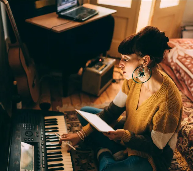 Girl with brown hair and fringe playing keyboard in bedroom